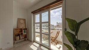 Una habitación con un gran ventanal corredizo que da a un balcón con vistas a edificios y una planta.