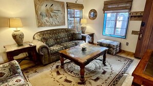 A living room with a ceiling fan, patterned sofa, coffee table, and decorative rugs.