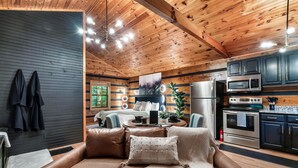 A cozy cabin interior with a leather sofa, wooden ceiling, and modern appliances.