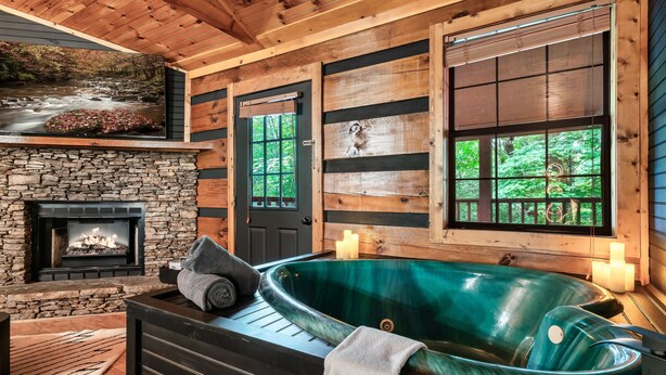 A spa area with a hot tub, a stone fireplace, and large windows with a view of greenery.