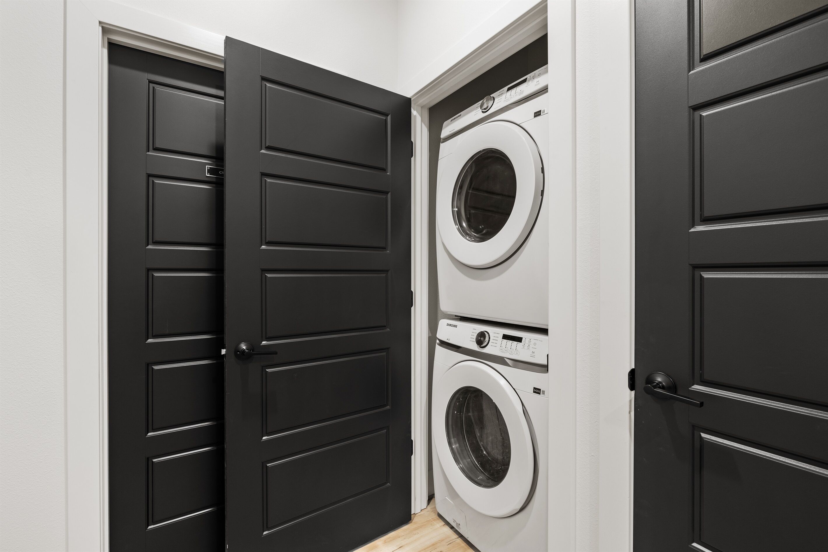 A laundry room with two stacked washing machines and a black door.