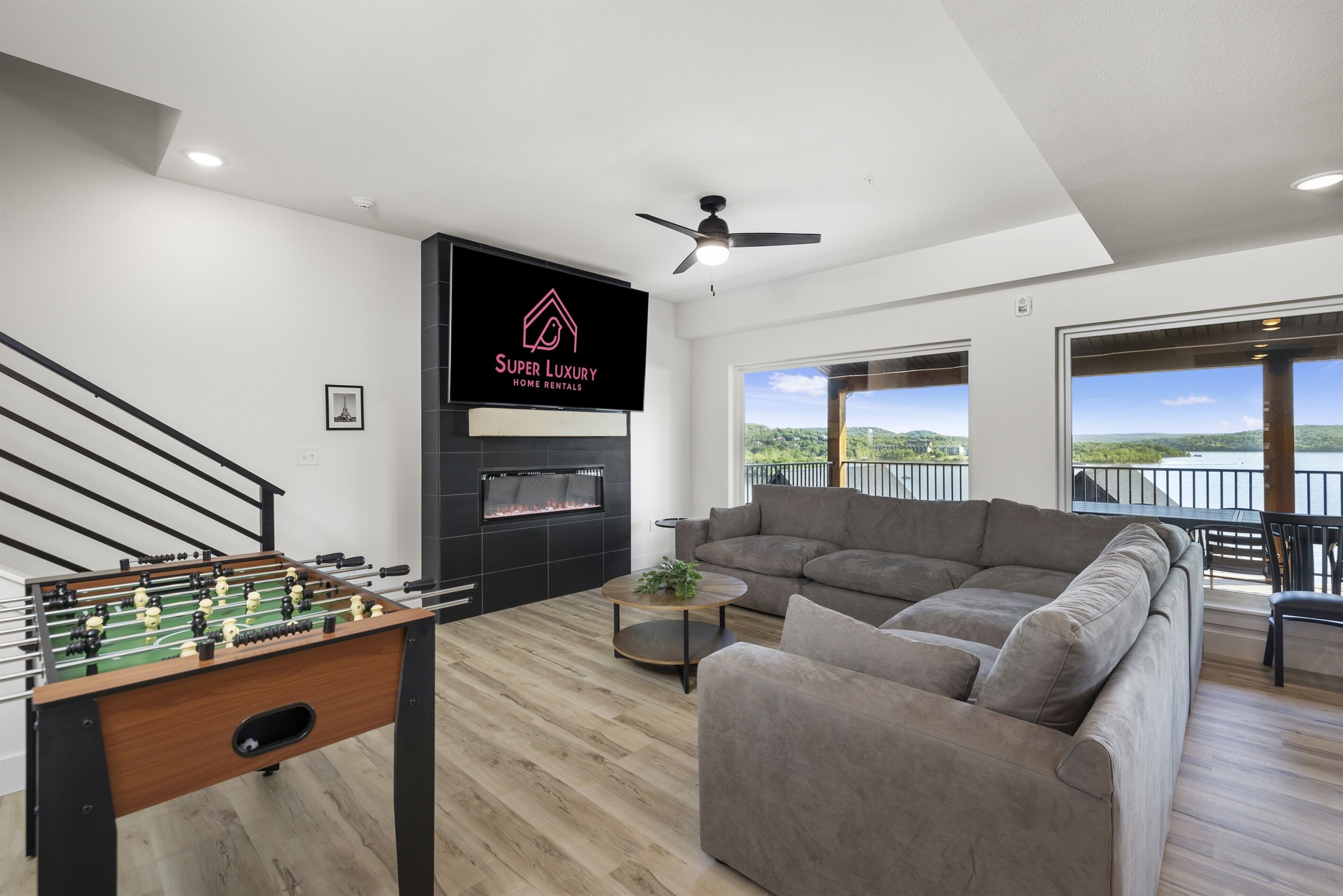 Un salón moderno con mesa de fútbol, un sofá grande color gris, chimenea y balcón con vistas.
