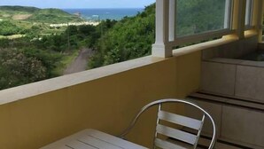 A balcony with a table and chair, overlooking a scenic landscape with greenery and a view of the sea. - South Sea House Luxurious Apt No 2 (Cap Estate, St. Lucia)