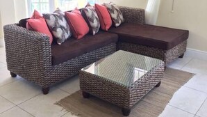 A living room with a wicker sofa, a glass coffee table, and a view of the outdoors through a window with sheer curtains. - South Sea House Luxurious Apt No 2 (Cap Estate, St. Lucia)