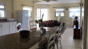 A kitchen with a granite countertop, white cabinets, a white refrigerator, and a dining area with a white table and chairs. - South Sea House Luxurious Apt No 2 (Cap Estate, St. Lucia)