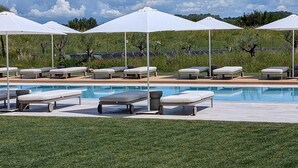 Un área junto a la piscina con sillas de descanso y sombrillas, cielo despejado y césped al frente.