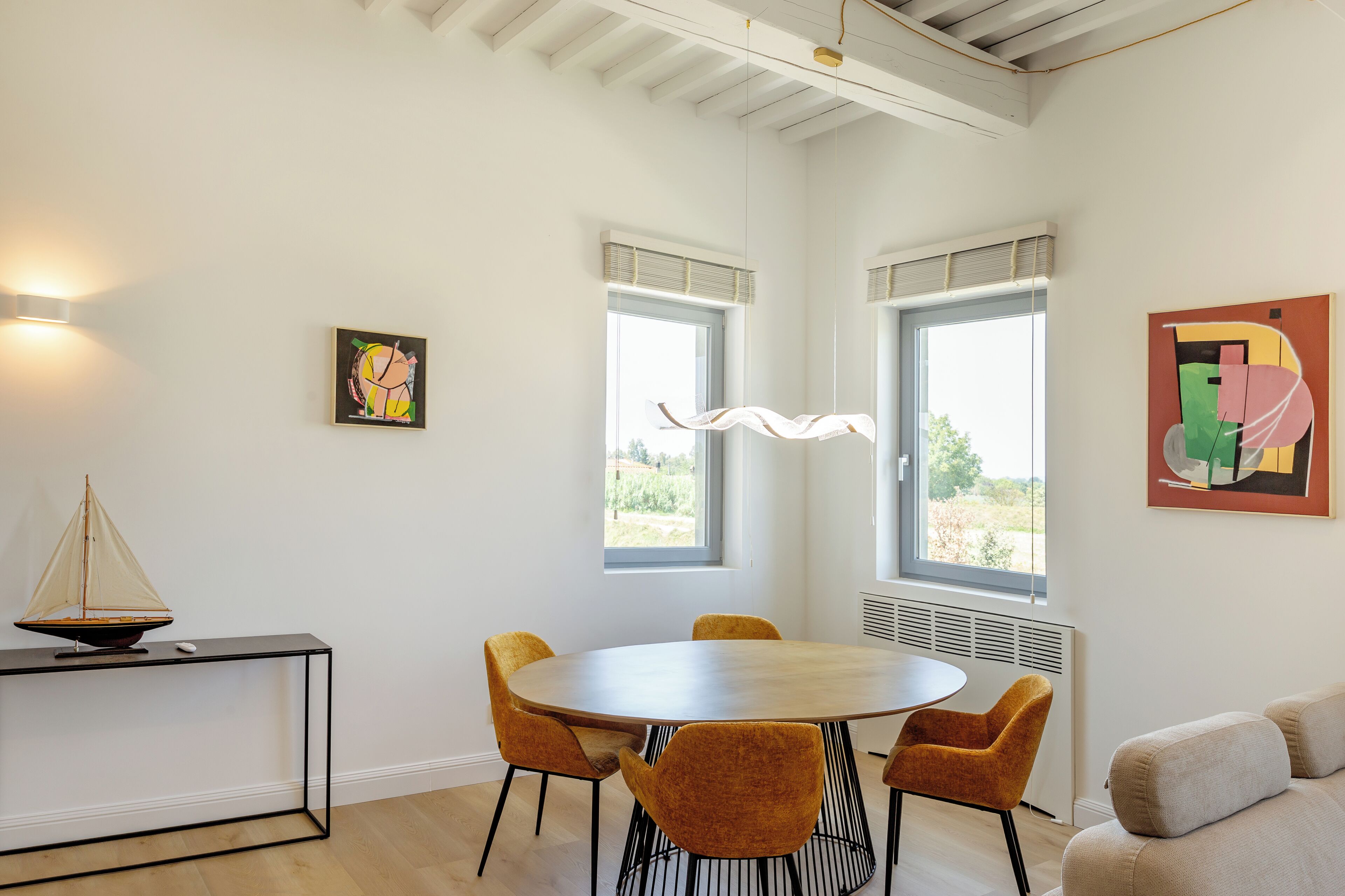 Un'area pranzo moderna con un tavolo rotondo, quattro sedie, un piccolo tavolo con un modellino di una barca a vela e opere d'arte alle pareti.