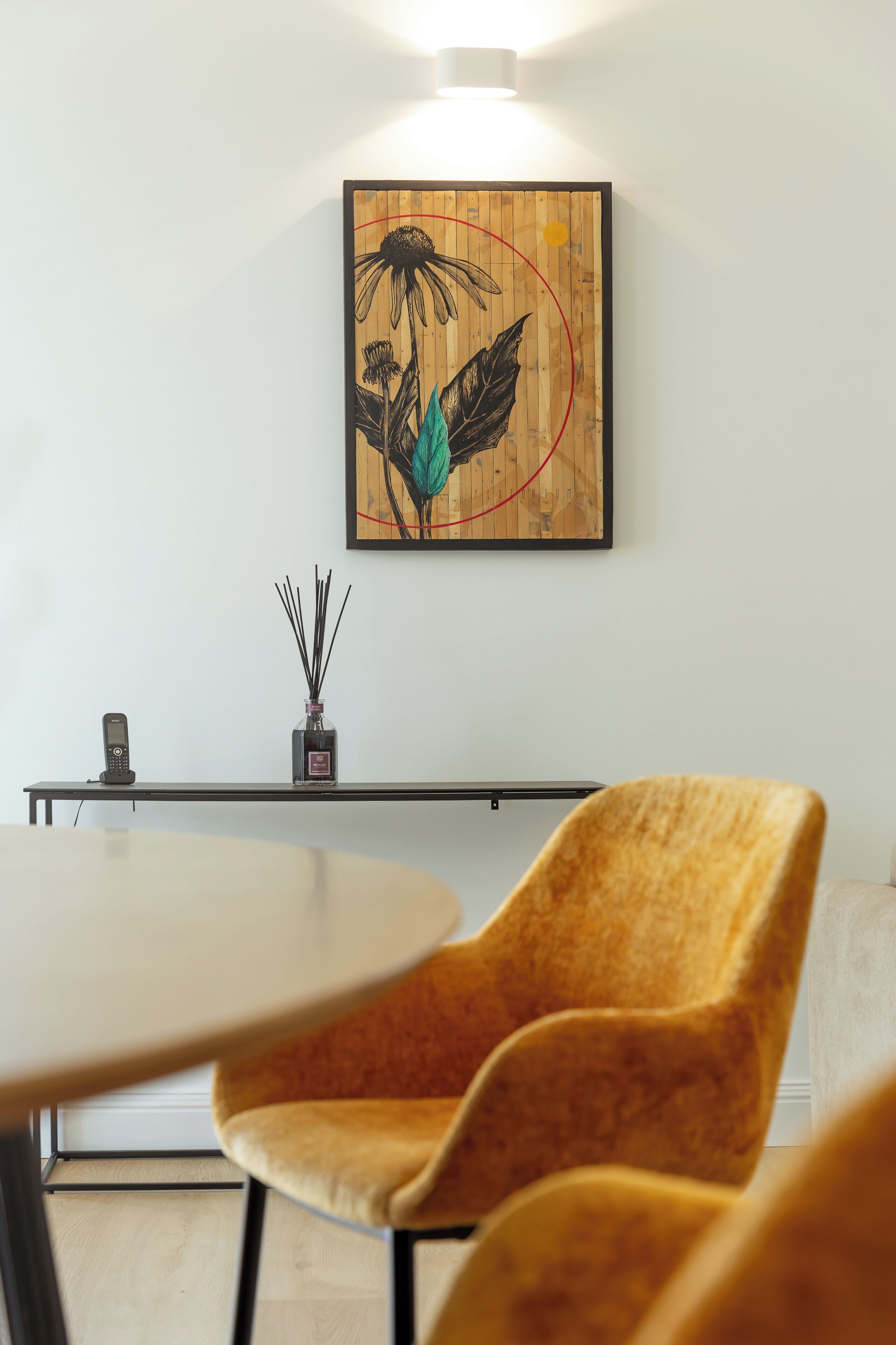 Une pièce avec une œuvre d’art murale en bois, une petite table sur laquelle est posé un vase, et une chaise jaune.