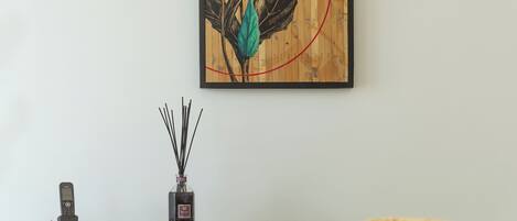 Une pièce avec une œuvre d’art murale en bois, une petite table sur laquelle est posé un vase, et une chaise jaune.