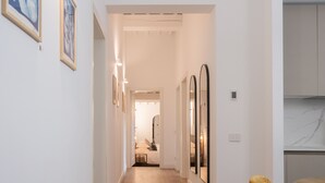 A hallway with a wooden floor, white walls, and framed artwork. There is a door leading to a room with a bed and a mirror. - Tenuta Asmara Luxury Resort (San Miniato)
