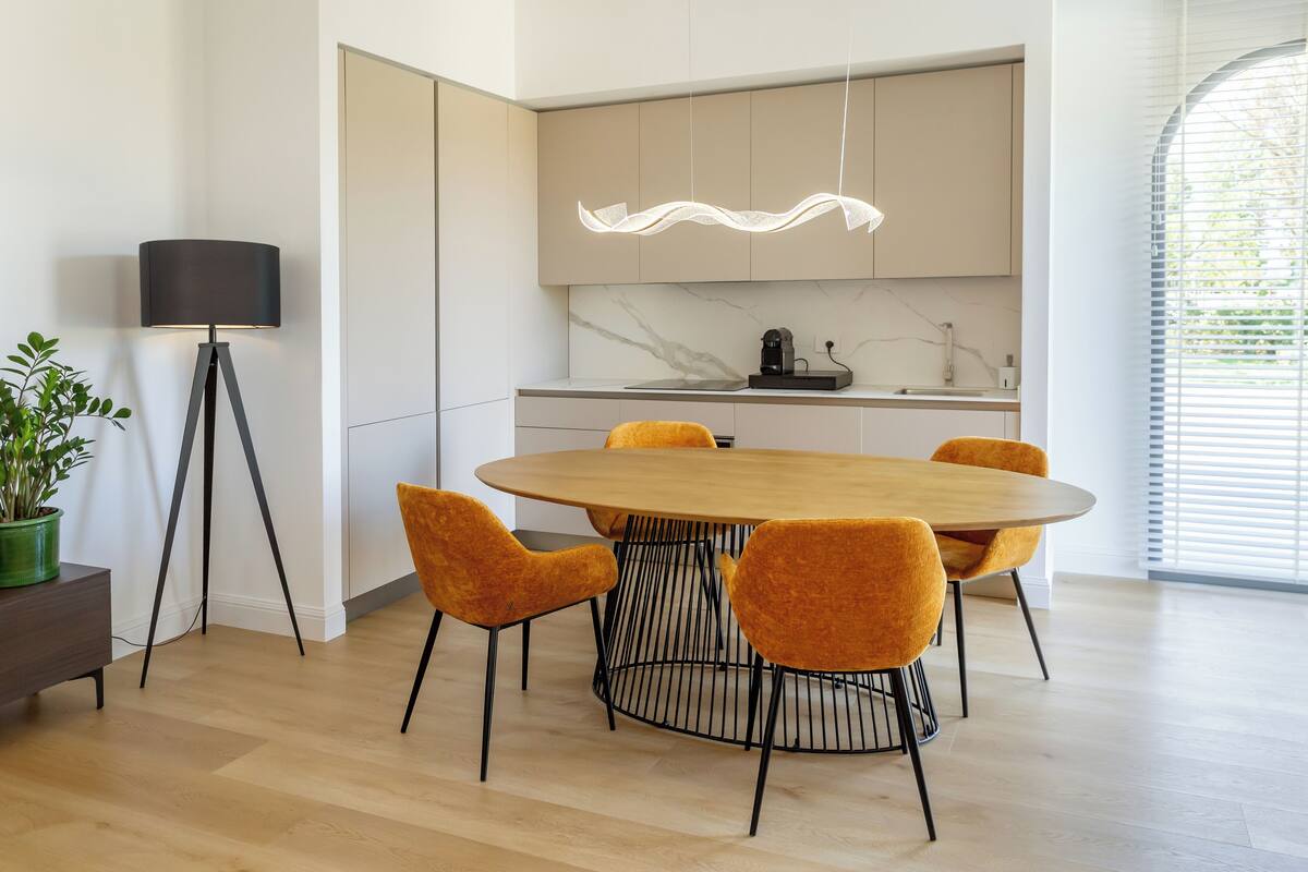 Una cocina moderna con encimera de mármol, una mesa redonda de madera y sillas color naranja.