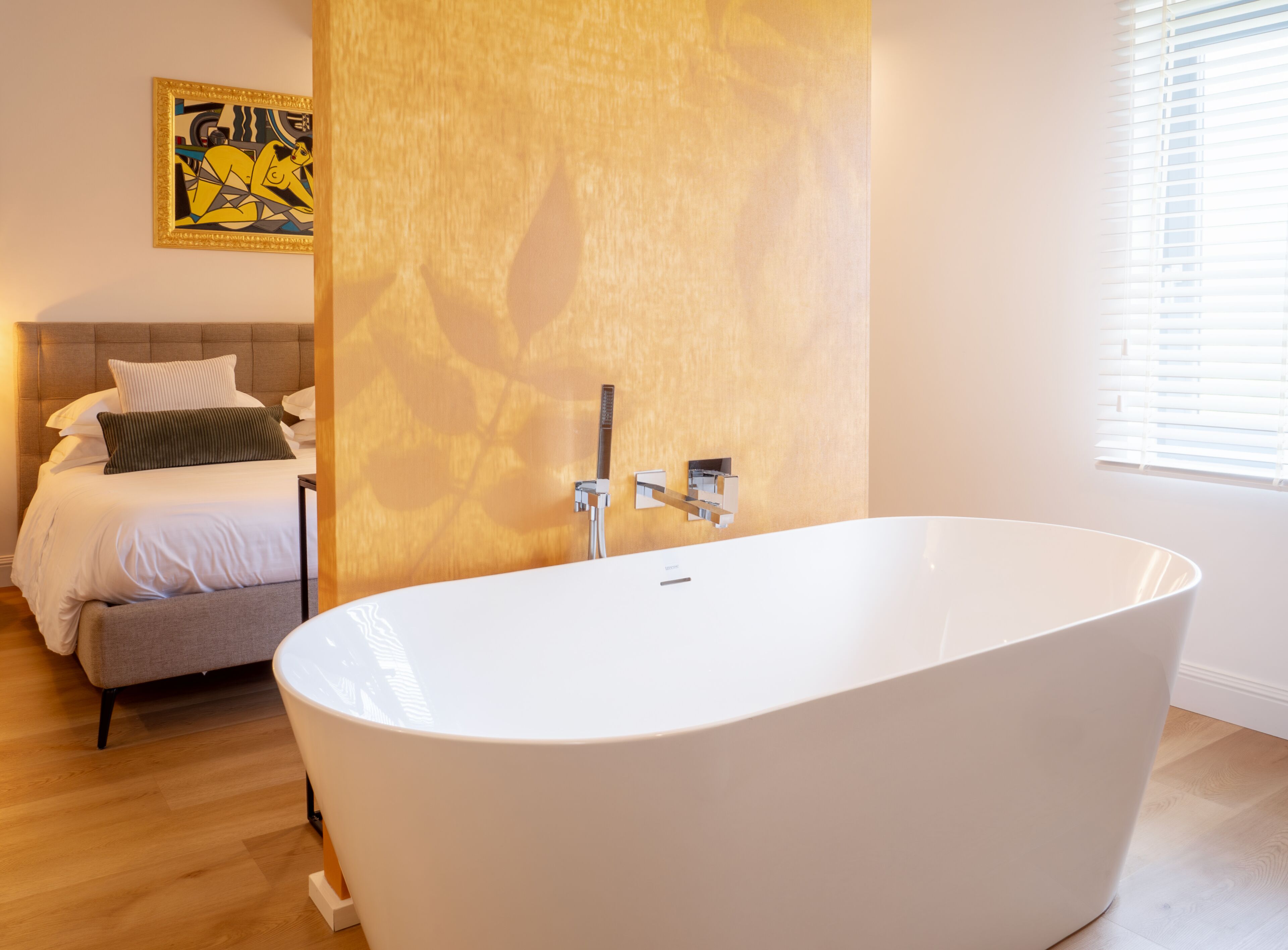 Een moderne badkamer met een vrijstaand bad, een bed met hoofdeinde, en een schilderij aan de muur.