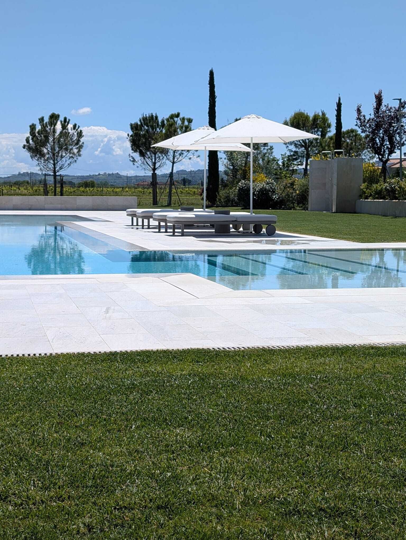 A swimming pool with lounge chairs and an umbrella, surrounded by grass and trees.