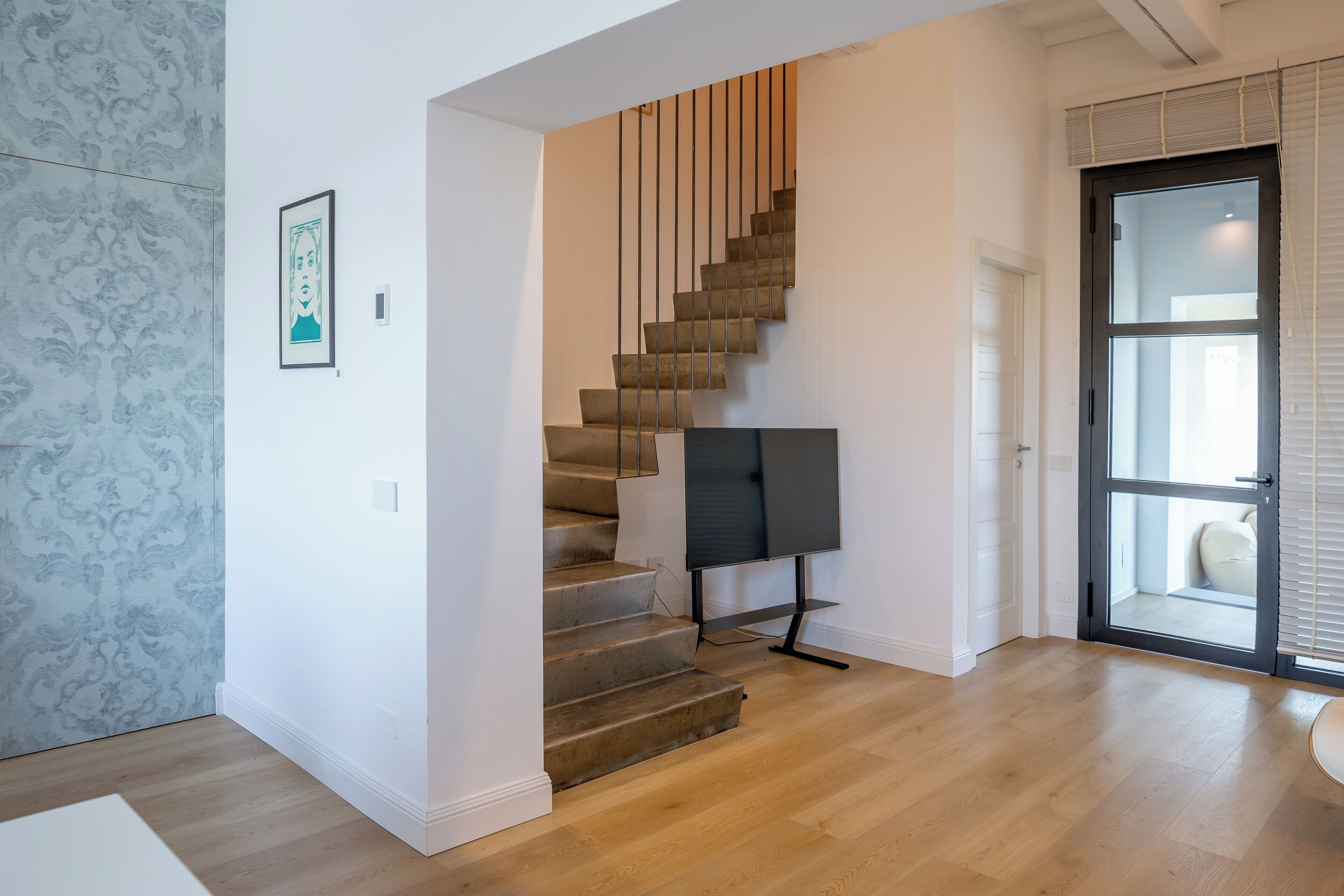 Een modern interieur met een houten trap, een ingelijst kunstwerk aan de muur en een deur naar buiten.
