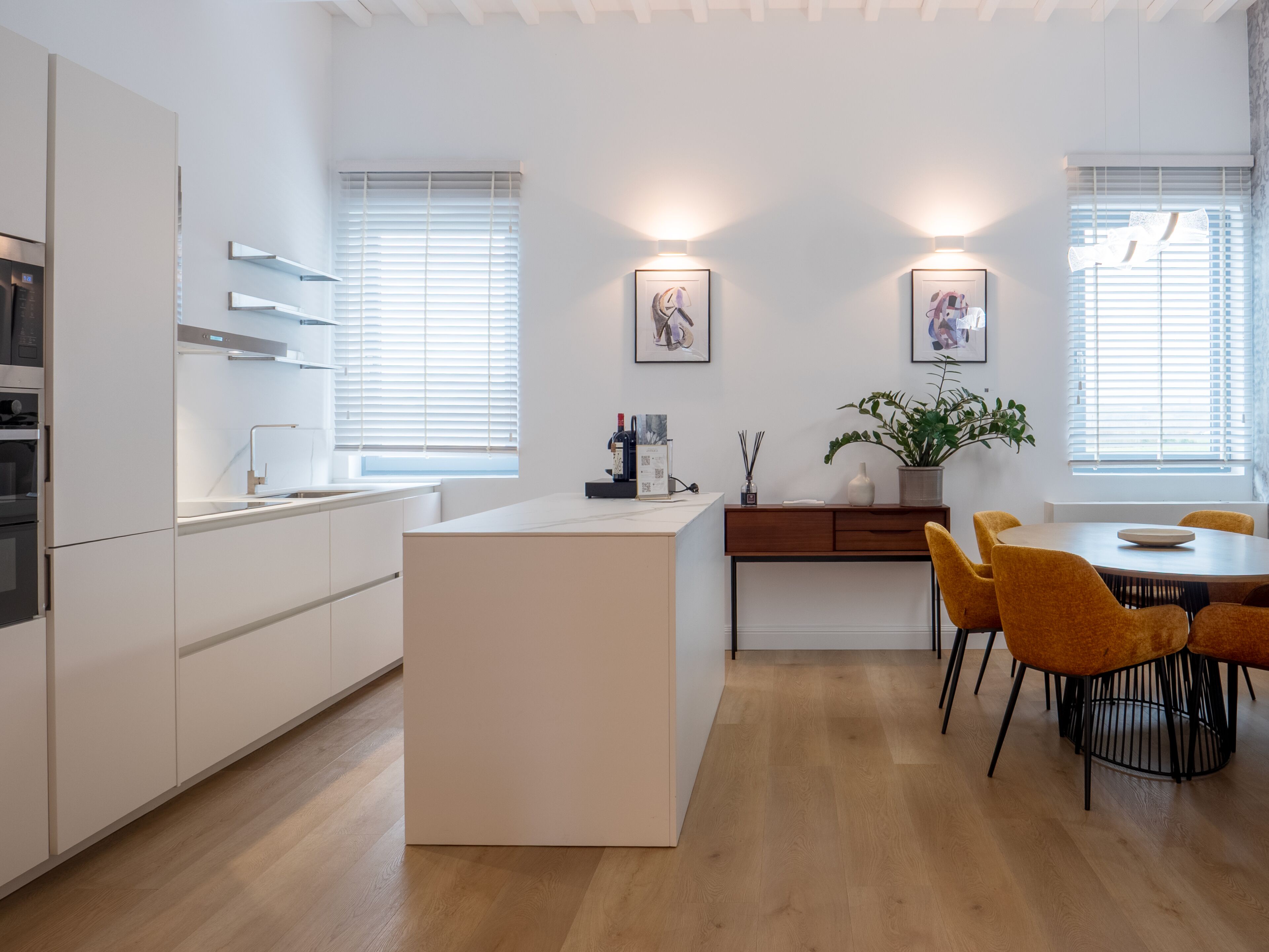 A modern kitchen with white cabinetry, a central island, and a dining area with yellow chairs.