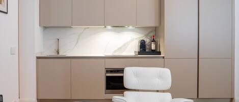 A modern kitchen with a marble countertop, a built-in oven, and a white chair.