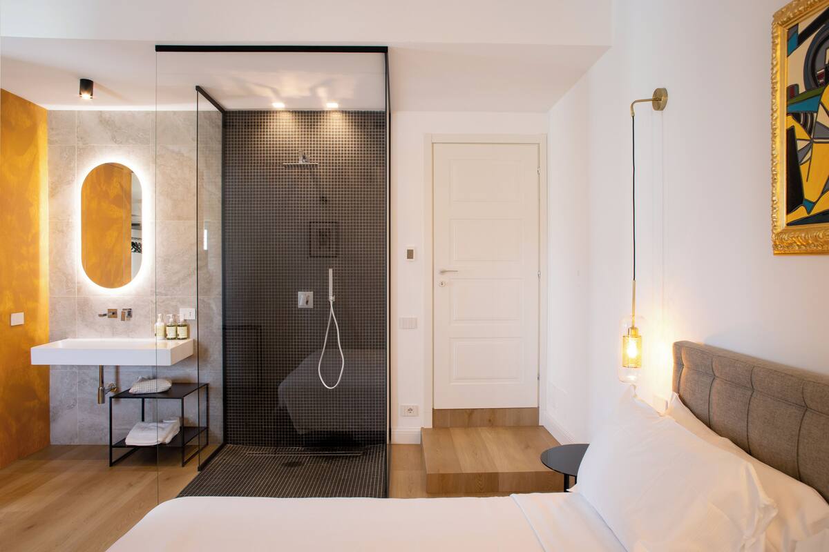 Un baño moderno con ducha de vidrio, un lavabo blanco y una mesita de noche con lámpara.