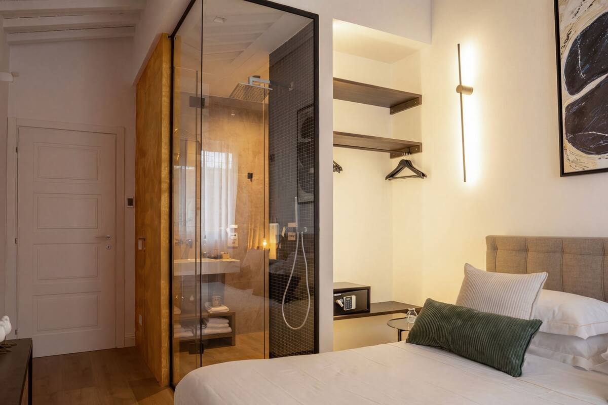 Una habitación de hotel con cama, mesita de noche, lámpara colgante, armario y zona de ducha.
