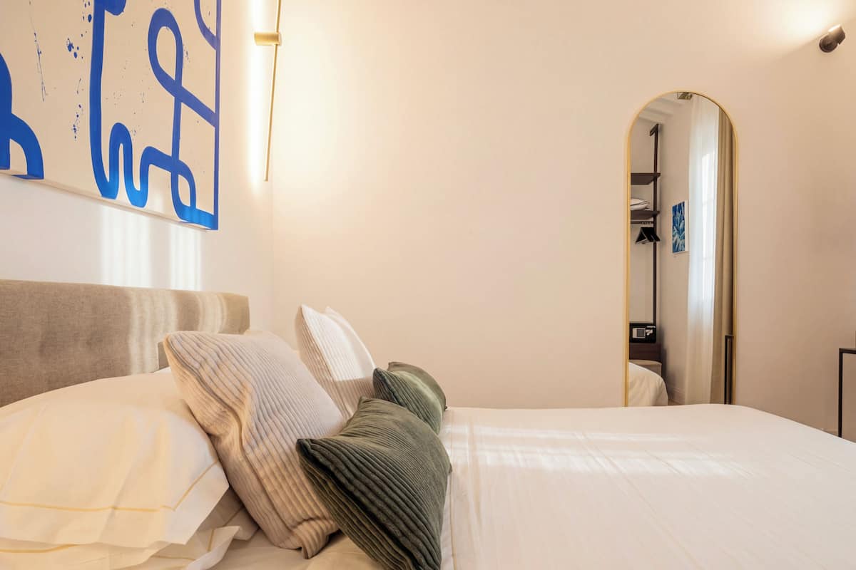 Una habitación de hotel con cama, almohadas, una pared con arte abstracto y un espejo.
