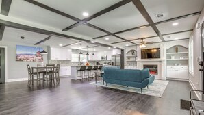 A spacious living area with a blue sofa, dining table, and chairs. There is a kitchen area with white cabinets and a microwave.