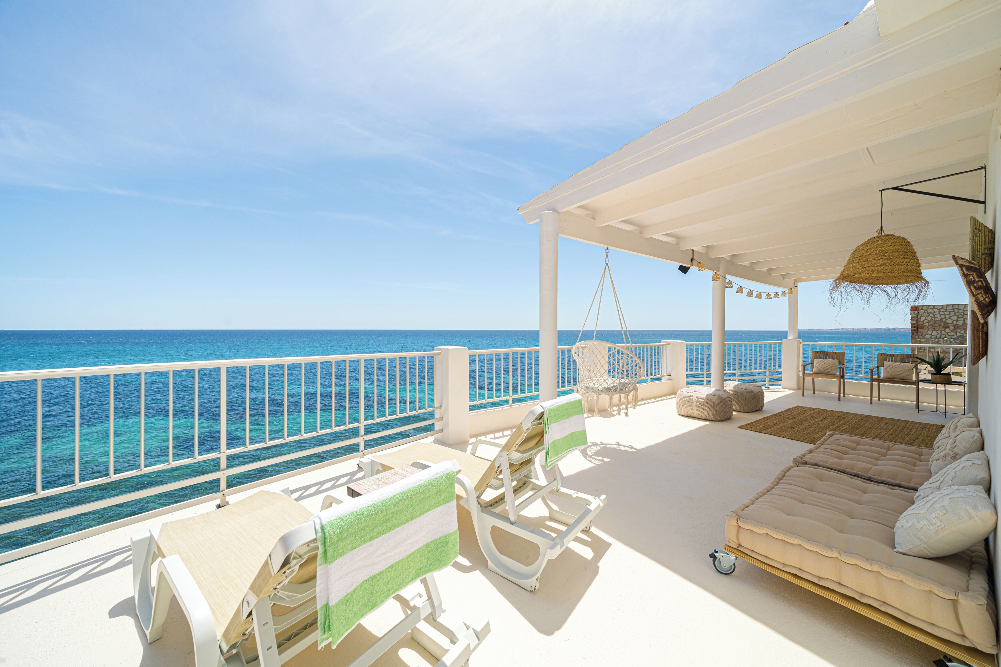 A sunlit outdoor seating area with a view of the sea, featuring a sofa, chairs, and a table.