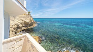 A coastal building with a balcony overlooking clear blue waters and a rocky shoreline. - Stunning Brand New Villa Sea View (la Coveta Fumada)