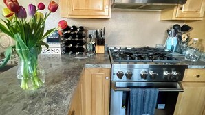 A kitchen with wooden cabinets, a gas stove, and a stainless steel oven. There is a vase with tulips on the counter.