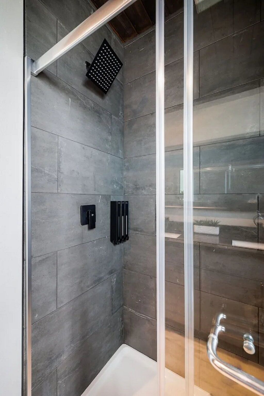 Une douche moderne avec une porte en verre, des murs recouverts de carreaux gris et un plafond en bois.