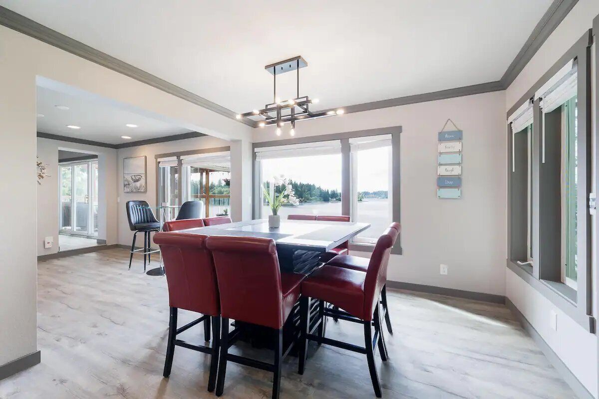 A spacious dining area with a large table and red chairs, large windows with views, and a modern ceiling light fixture.