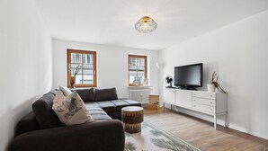 Un salon moderne avec un canapé d’angle, un téléviseur à écran plat, un meuble blanc et un tapis décoratif.