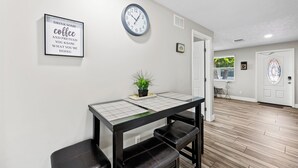 Un intérieur épuré et moderne, avec un plancher en bois, une horloge, une citation encadrée accrochée au mur et une petite plante posée sur une table.