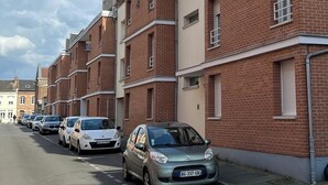 En rad hus med röda tegelstensfasader, som används som lägenhetsbyggnader, och parkerade bilar längs gatan.