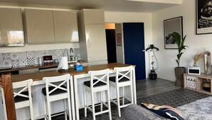 Ett modernt kök med en bardisk, vita stolar och en grå soffa.