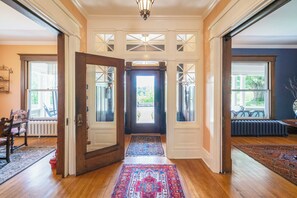 A spacious entryway with a wooden floor, a patterned rug, and a view through the door to an outdoor area. - Lion's Head Bed & Breakfast (Niagara Falls)
