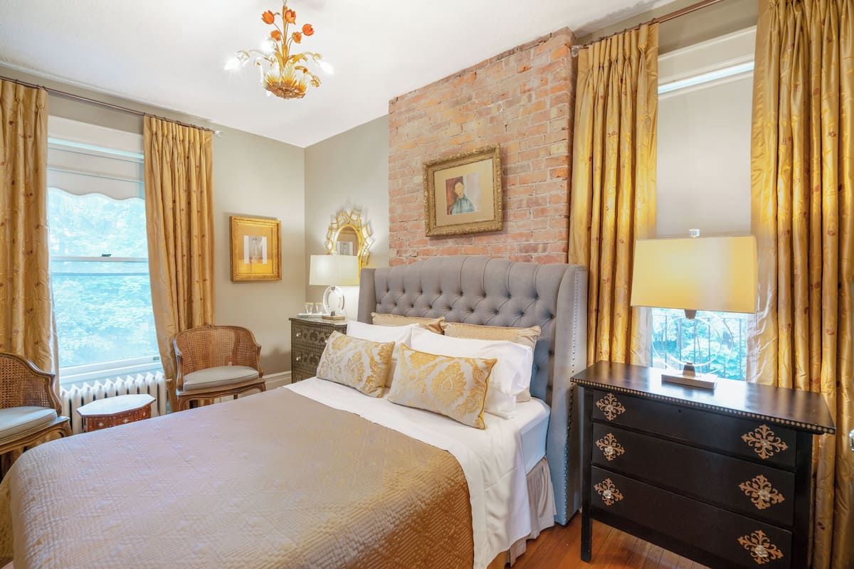 A bedroom with a large bed, a dresser, a chair, a nightstand, and a view of the sea.