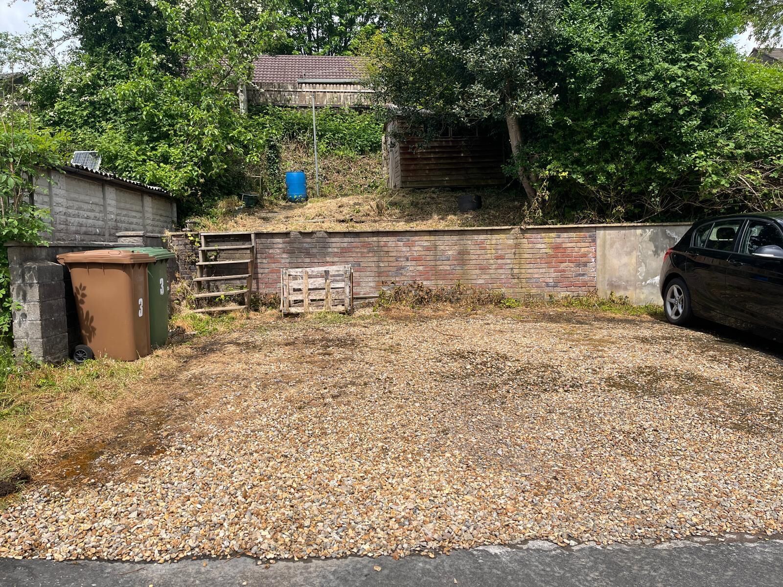 A gravel driveway leading to a wooden fence and a brick wall.