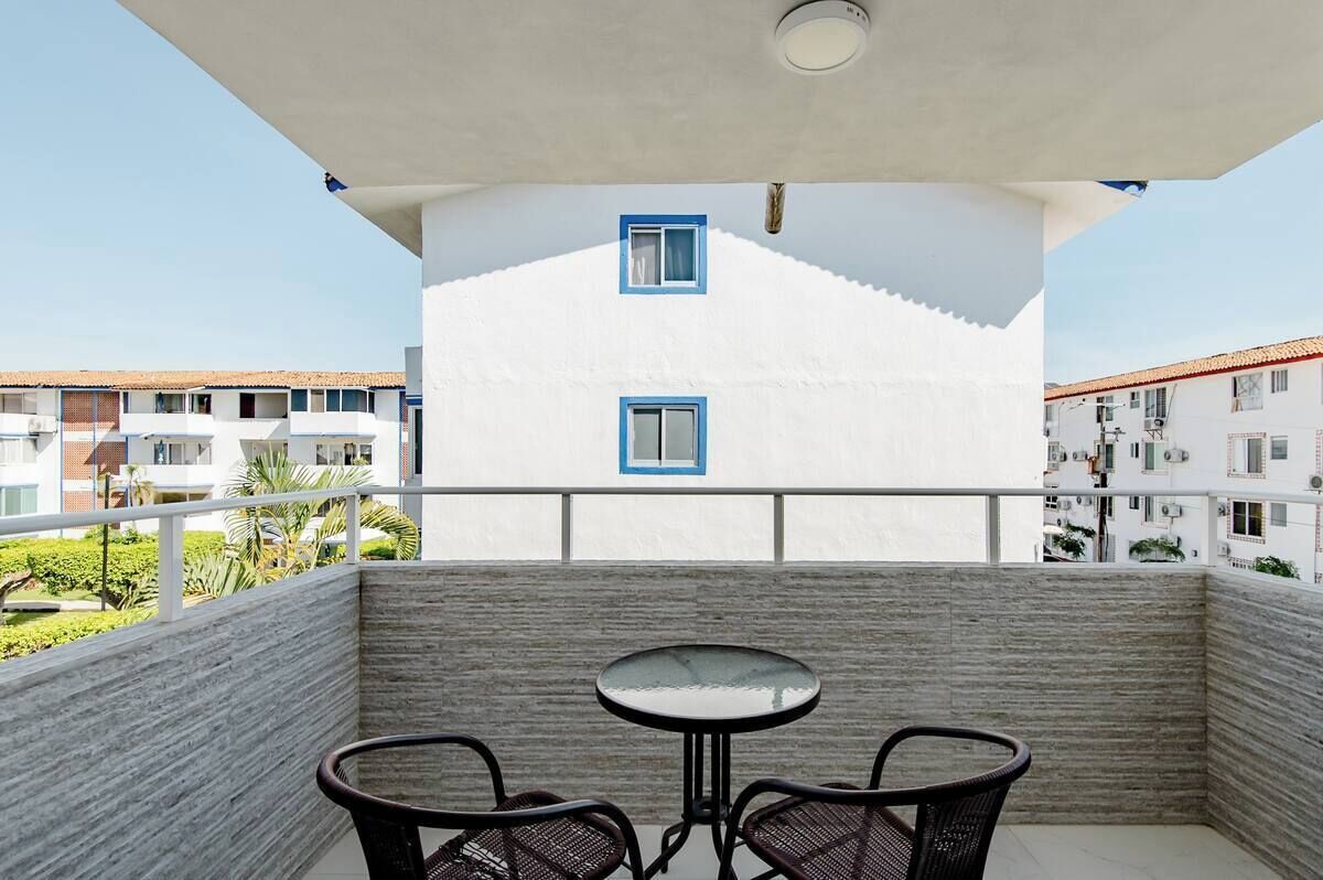 A balcony with a table and chairs, white walls, and blue-framed windows.