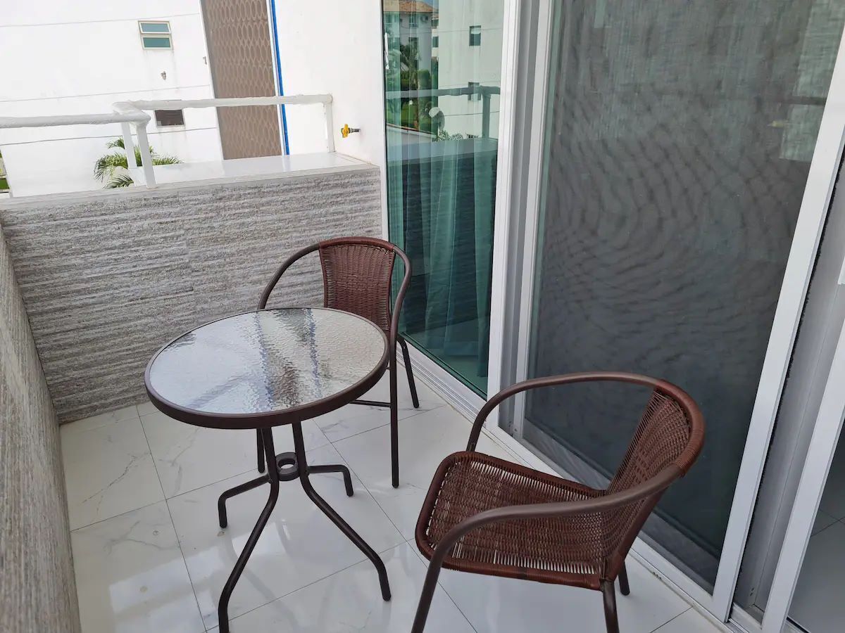 A balcony with a glass door, two wicker chairs, and a glass-top table.