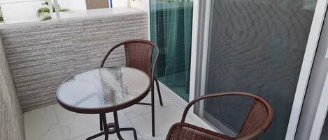 A balcony with a glass door, two wicker chairs, and a glass-top table.