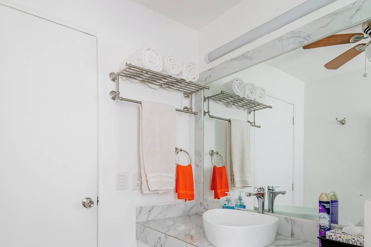 Een moderne badkamer met een witte wastafel, een grote spiegel en een handdoekrek met witte en oranje handdoeken.