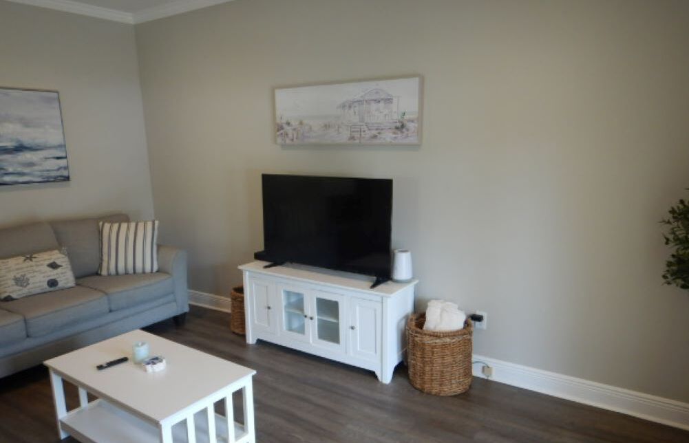 A living room with a grey sofa, a white coffee table, a TV on a white cabinet, and a painting on the wall.