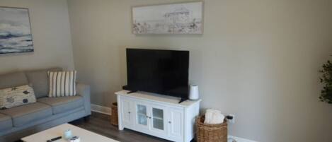 A living room with a grey sofa, a white coffee table, a TV on a white cabinet, and a painting on the wall.