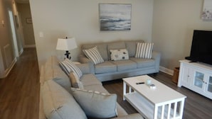 Een woonkamer met een bank, salontafel, televisie en een schilderij aan de muur.