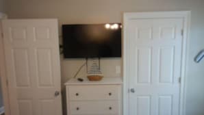 Een kamer met een witte ladekast, een flatscreen televisie erboven en een gesloten deur aan de rechterkant.