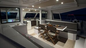 Un intérieur de yacht moderne comprenant un coin repas, une petite cuisine et de grandes fenêtres offrant une vue sur la mer.