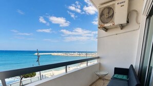 En balkong med utsikt över havet, ett litet bord, en soffa och en luftkonditioneringsanläggning.