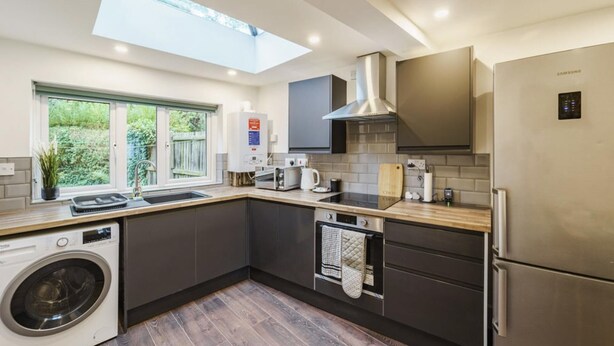 A modern kitchen with a built-in washing machine, a stainless steel refrigerator, and a skylight above the sink.