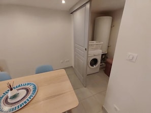 Una habitación pequeña con lavadora, una puerta que da a otra estancia y una mesa con un plato decorativo.