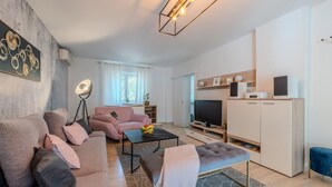 A modern living room with a sofa, ottoman, and coffee table, a television, and a cabinet with electronic devices.