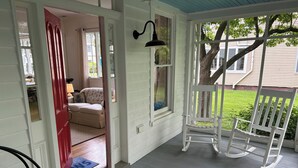A porch with a rocking chair, a door leading to a room with a sofa, and a view of a house and tree. - 3-bedroom historic vacation home newly renovated in the middle of Oxford MD. (Oxford)